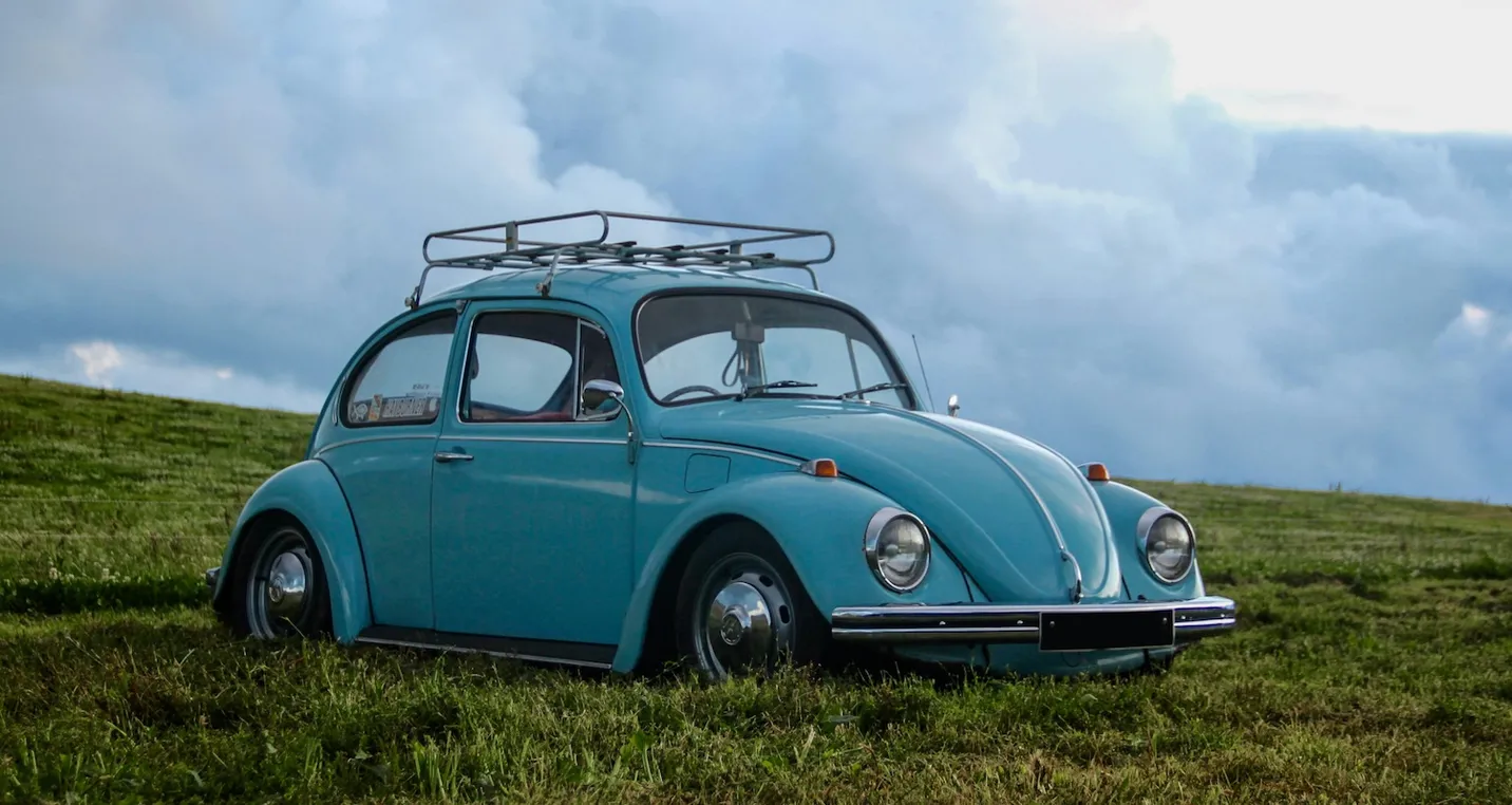 Old Blue Volkswagen Beetle parked in a field on a cloudy day