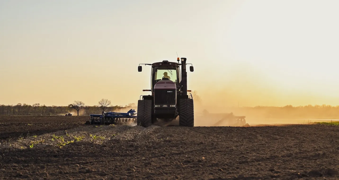 A farmer plowing his field with his tractor on a sunny day at sunset