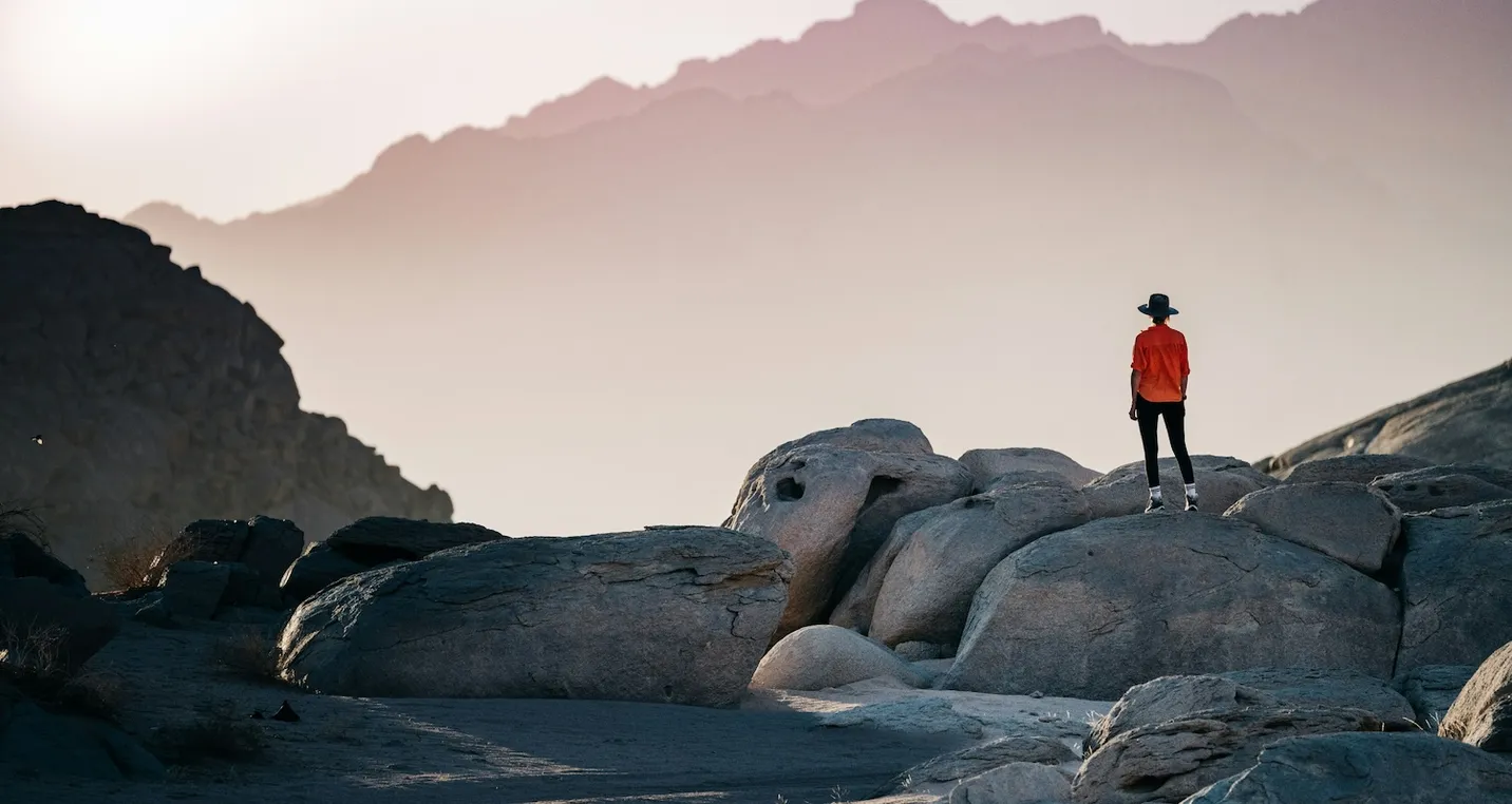 A Woman in a red dress standing on a rocks overlooking the ocean.