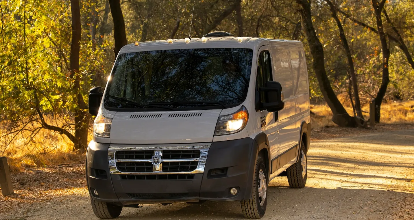 White van parked driving on a road in mid summer surrounded by trees