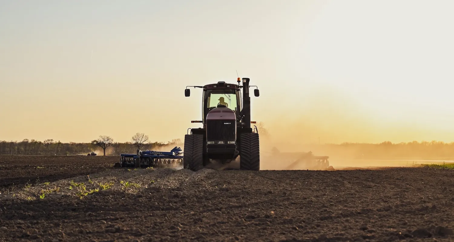 A farmer plowing his field with his tractor on a sunny day at sunset